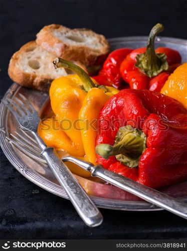 Fresh roasted red and yellow peppers on vintage plate over dark background, selective focus