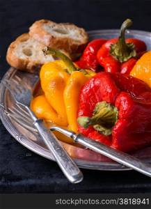 Fresh roasted red and yellow peppers on vintage plate over dark background, selective focus