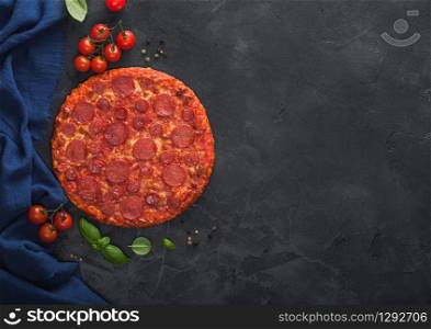Fresh round baked Hot and Spicy Pepperoni pizza with tomatoes with basil on black kitchen table background.