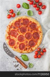 Fresh round baked Pepperoni italian pizza with knife with tomatoes and basil on kitchen table background.