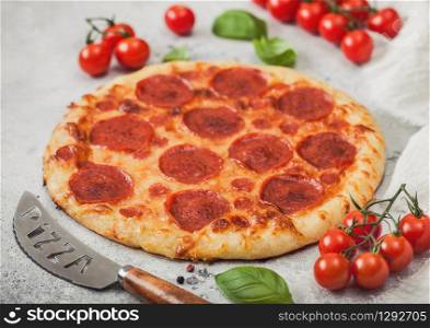 Fresh round baked Pepperoni italian pizza with knife with tomatoes and basil on kitchen table background.