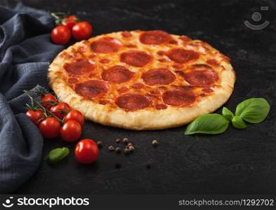 Fresh round baked Pepperoni italian pizza with tomatoes with basil on black kitchen table background.