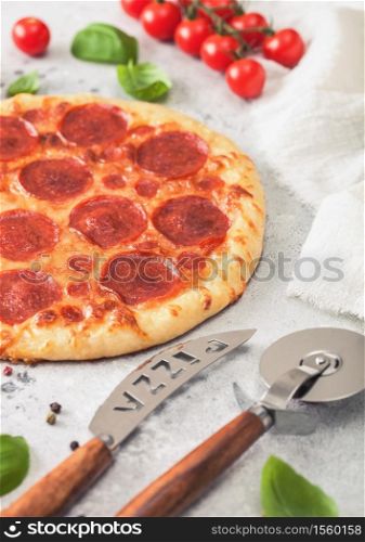 Fresh round baked Pepperoni italian pizza with wheel cutter and knife with tomatoes and basil on light kitchen table background.