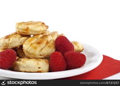 Fresh round dessert pastries garnished with ripe red raspberries on white plate over white background with copy space.