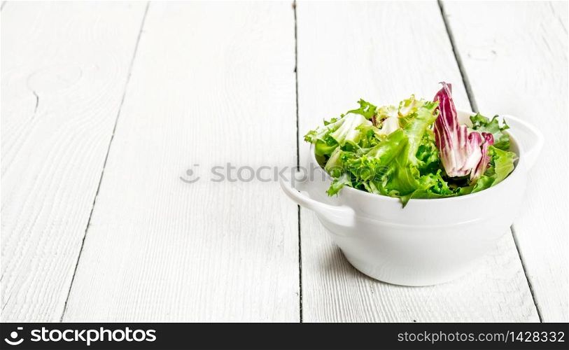 Fresh salad greens in a bowl. On a white wooden background.. Fresh salad greens in a bowl.