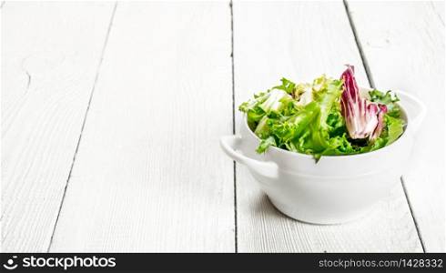 Fresh salad greens in a bowl. On a white wooden background.. Fresh salad greens in a bowl.