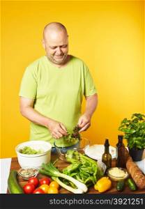 Fresh salad ingredients on the table, middle-aged man cook salad and used salad spin dryer - copy space and yellow background