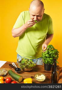Fresh salad ingredients on the table, middle-aged man sniffs basil leaves - copy space and yellow background