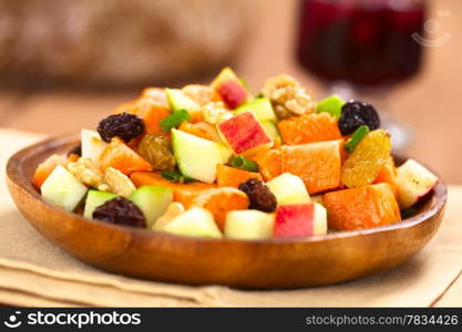 Fresh salad made of cooked sweet potatoes, fresh apples, nuts, raisins and shallots on wooden plate with mulled wine in the back (Selective Focus, Focus one third into the salad). Sweet Potato and Apple Salad