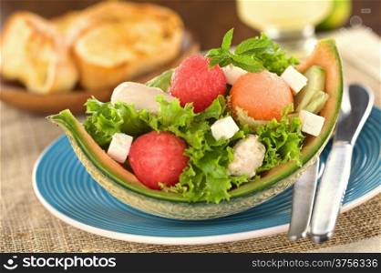 Fresh salad made of watermelon, cantaloupe melon, chicken, cucumber, cheese and lettuce (Selective Focus, Focus on the front of the mint leaf and the two melon balls below it)