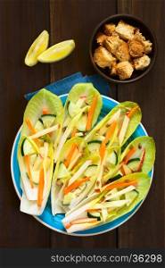 Fresh salad of endive leaves, cucumber, carrot, apple and sunflower seeds, croutons and lemon wedges above, photographed overhead with natural light