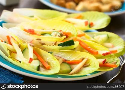 Fresh salad of endive leaves, cucumber, carrot, apple and sunflower seeds, photographed with natural light (Selective Focus, Focus in the middle of the image)
