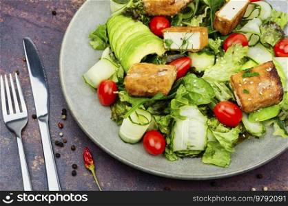 Fresh salad of greens, cucumber, avocado, tomatoes and breaded fried tofu soy cheese in a plate. Vegetarian food. Healthy salad of frying tofu cheese and fresh vegetables.