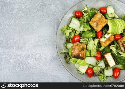 Fresh salad of greens, cucumber, avocado, tomatoes and breaded fried tofu soy cheese. Vegetarian food, copy space. Healthy salad of grilled tofu cheese and fresh vegetables.