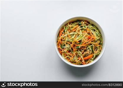 Fresh salad of sliced thin strips of carrot and zucchini on a concrete background. Vegetarian cuisine. Fresh salad of sliced thin strips of carrot and zucchini on a concrete background