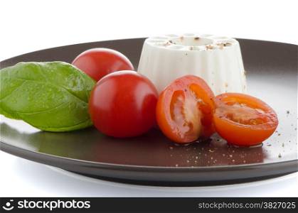 Fresh salad with goat cheese, tomato and basil pesto on a brown plate.