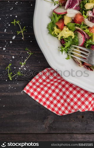 Fresh salad with mixed greens, radish, cheese and tomato in a plate on wooden background. Italian Mediterranean or Greek cuisine. Vegetarian vegan food. Fresh salad with mixed greens, radish, cheese and tomato in a plate on wooden background. Italian Mediterranean or Greek cuisine. Vegetarian vegan food. Top view