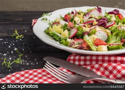 Fresh salad with mixed greens, radish, cheese and tomato in a plate on wooden background. Italian Mediterranean or Greek cuisine. Vegetarian vegan food