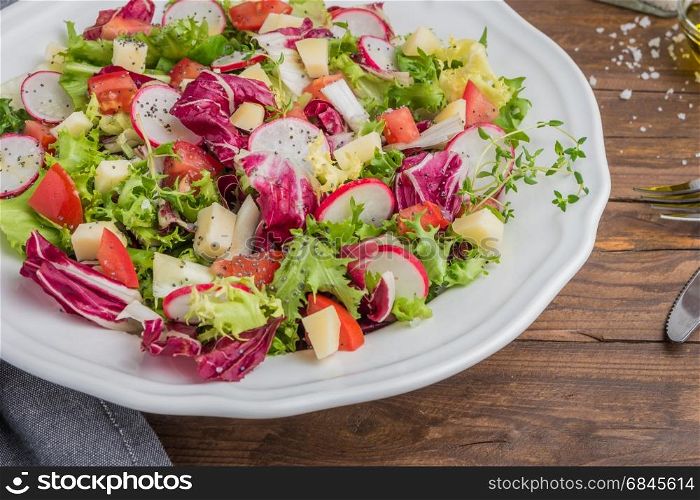 Fresh salad with mixed greens, radish, cheese and tomato in a plate on wooden background. Italian Mediterranean or Greek cuisine. Vegetarian vegan food
