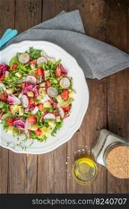 Fresh salad with mixed greens radish cheese and tomato in a plate on wooden background. Italian Mediterranean or Greek cuisine. Vegetarian vegan food.