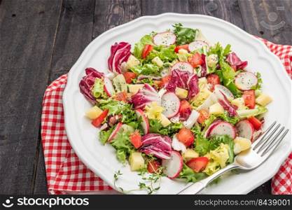 Fresh salad with mixed greens radish cheese and tomato in a plate on wooden background. Italian Mediterranean or Greek cuisine. Vegetarian vegan food.