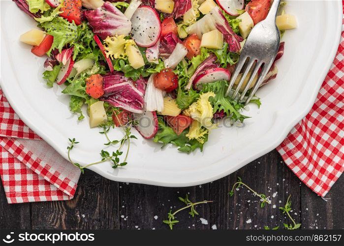 Fresh salad with mixed greens, radish, cheese and tomato in a plate on wooden background. Italian Mediterranean or Greek cuisine. Vegetarian vegan food. Top view