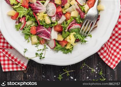Fresh salad with mixed greens, radish, cheese and tomato in a plate on wooden background. Italian Mediterranean or Greek cuisine. Vegetarian vegan food. Top view