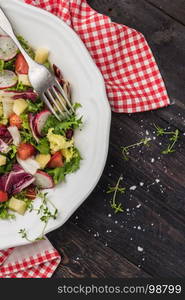 Fresh salad with mixed greens, radish, cheese and tomato in a plate on wooden background. Italian Mediterranean or Greek cuisine. Vegetarian vegan food. Top view