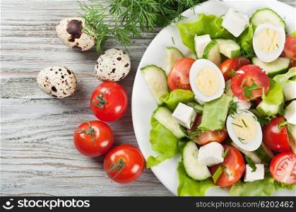 Fresh salad with quail eggs, cherry tomato, cucumber and lettuce on a wooden background. Top view.