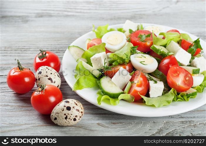 Fresh salad with quail eggs, cherry tomato, cucumber and lettuce on a wooden background
