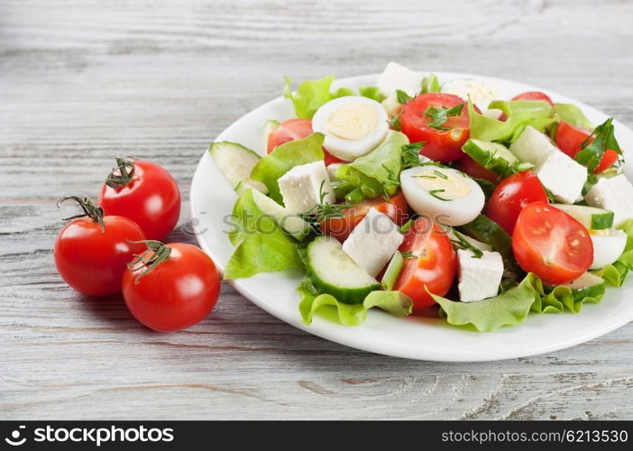 Fresh salad with quail eggs, cherry tomato, cucumber and lettuce on a wooden table