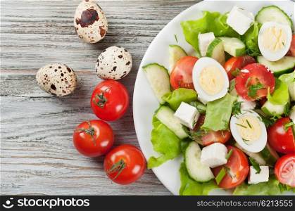 Fresh salad with quail eggs, cherry tomato, cucumber and lettuce on a wooden table. Top view.