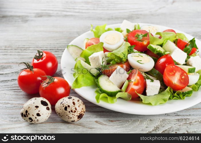 Fresh salad with quail eggs, cherry tomato, cucumber and lettuce on a wooden table.