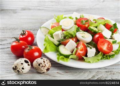 Fresh salad with quail eggs, cherry tomato, cucumber and lettuce on a wooden table.