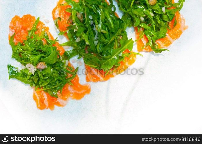 fresh salmon carpaccio sushi sashimi with arugula rocket salad and caper on top