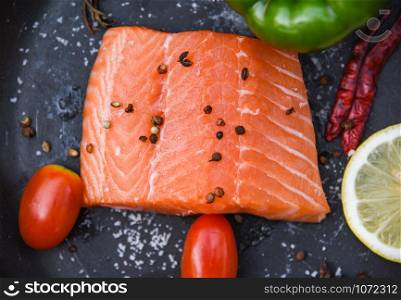 Fresh salmon fillet on dark background / Close up of raw salmon fish seafood with tomato lemon herbs and spices - top view