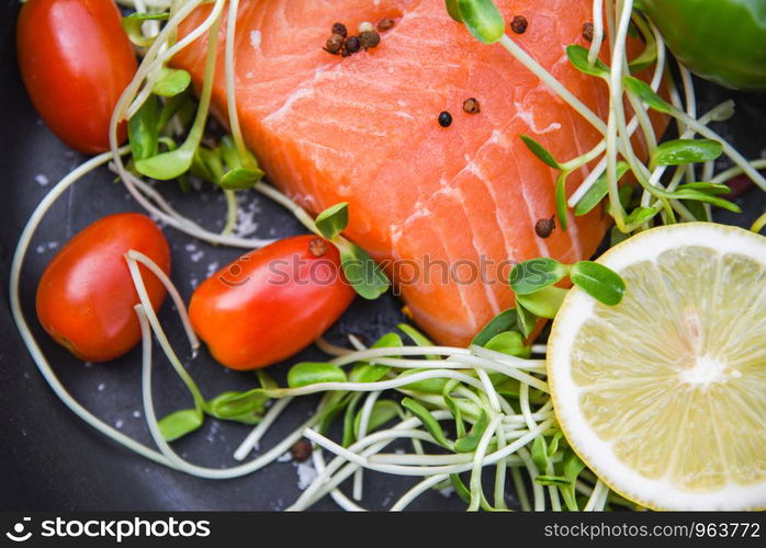 Fresh salmon fillet on dark background / Close up of raw salmon fish seafood with tomato lemon herbs spices and sunflower sprout