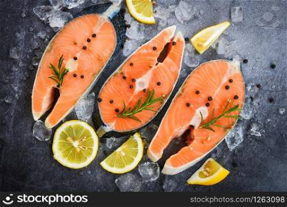 Fresh salmon steak with herbs and spices lemon rosemary on black plate background / Raw salmon fish fillet and ice for cooked steak seafood , top view