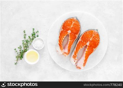 Fresh salmon steaks with ingredients for cooking on white board, view from above