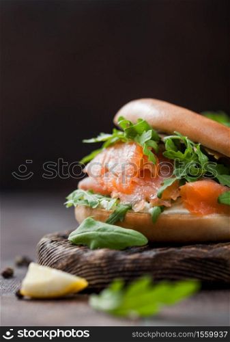 Fresh sandwich with salmon and bagel, wild rocket and cream cheese with lemon and pepper on wood.