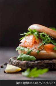 Fresh sandwich with salmon and bagel, wild rocket and cream cheese with lemon and pepper on wood.