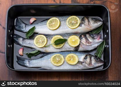 fresh sea bass pready for cooking in the pan with lemon slices and sage