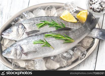 Fresh sea bass with rosemary and lime wedges on the metal tray