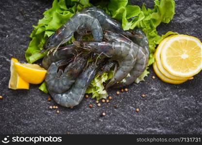 Fresh shrimp prawns uncooked with spices lemon and vegetable salad lettuce or green oak on dark background / Raw shrimps