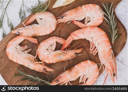 Fresh shrimps on wooden cutting board with herbs and spices rosemary on table background, boiled shrimp prawns cooked in the seafood restaurant