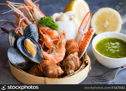Fresh shrimps prawns squid mussels spotted babylon shellfish crab and seafood sauce lemon on plate black stone background / Cooked steamer food served seafood buffet concept