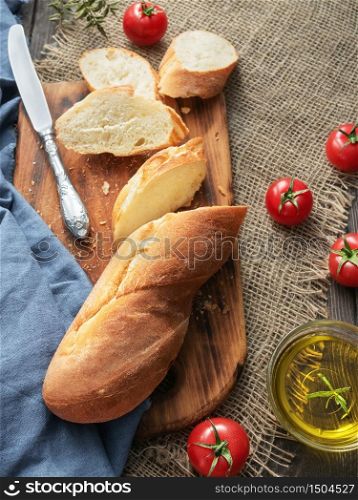 Fresh sliced baguette, tomatoes and olive oil, ingredients for making a sandwich, closeup. Rough fabric background