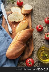 Fresh sliced baguette, tomatoes and olive oil, ingredients for making a sandwich, closeup. Rough fabric background