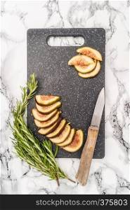 Fresh sliced figs, rosemary and knife on cutting board. Top view