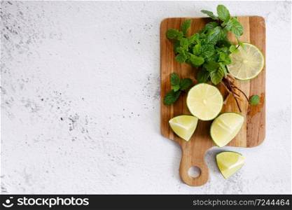 fresh sliced limes and fresh green mint leaves, making cocktail or lemonade, on wooden board. Top view.